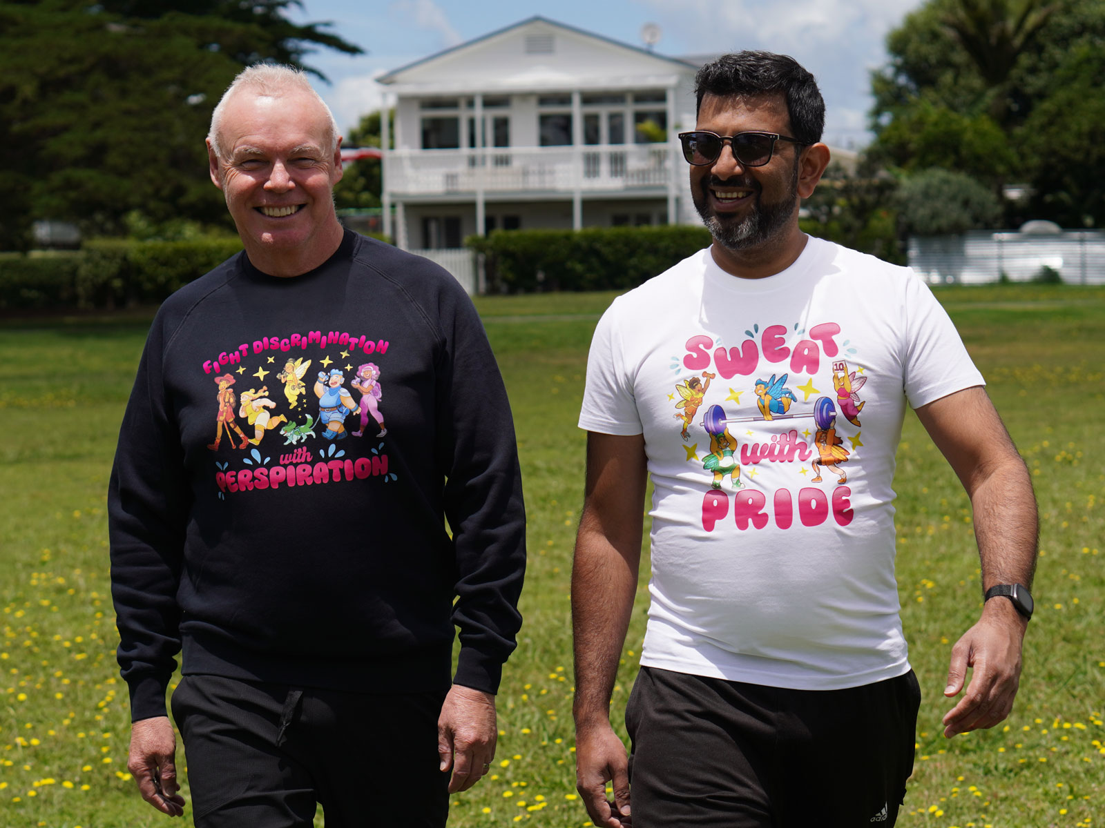 Photo showing two people walking in a park. One is wearing a Sweat with Pride sweater, the other is wearing a Sweat with Pride t-shirt.