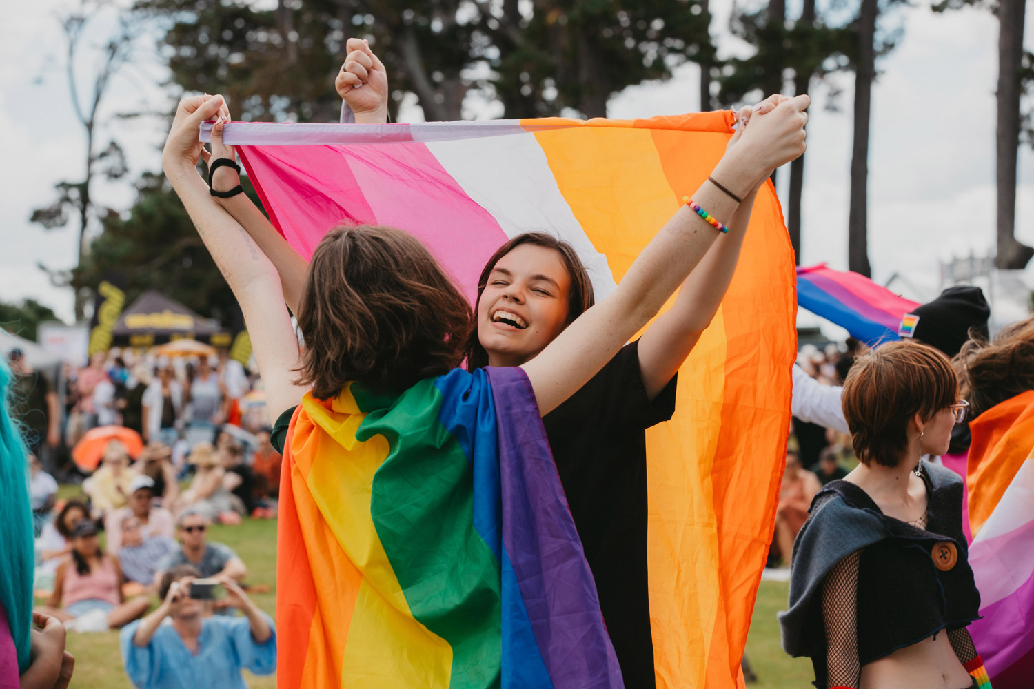 Photo of two people at Big Gay Out, hugging, with pride flags