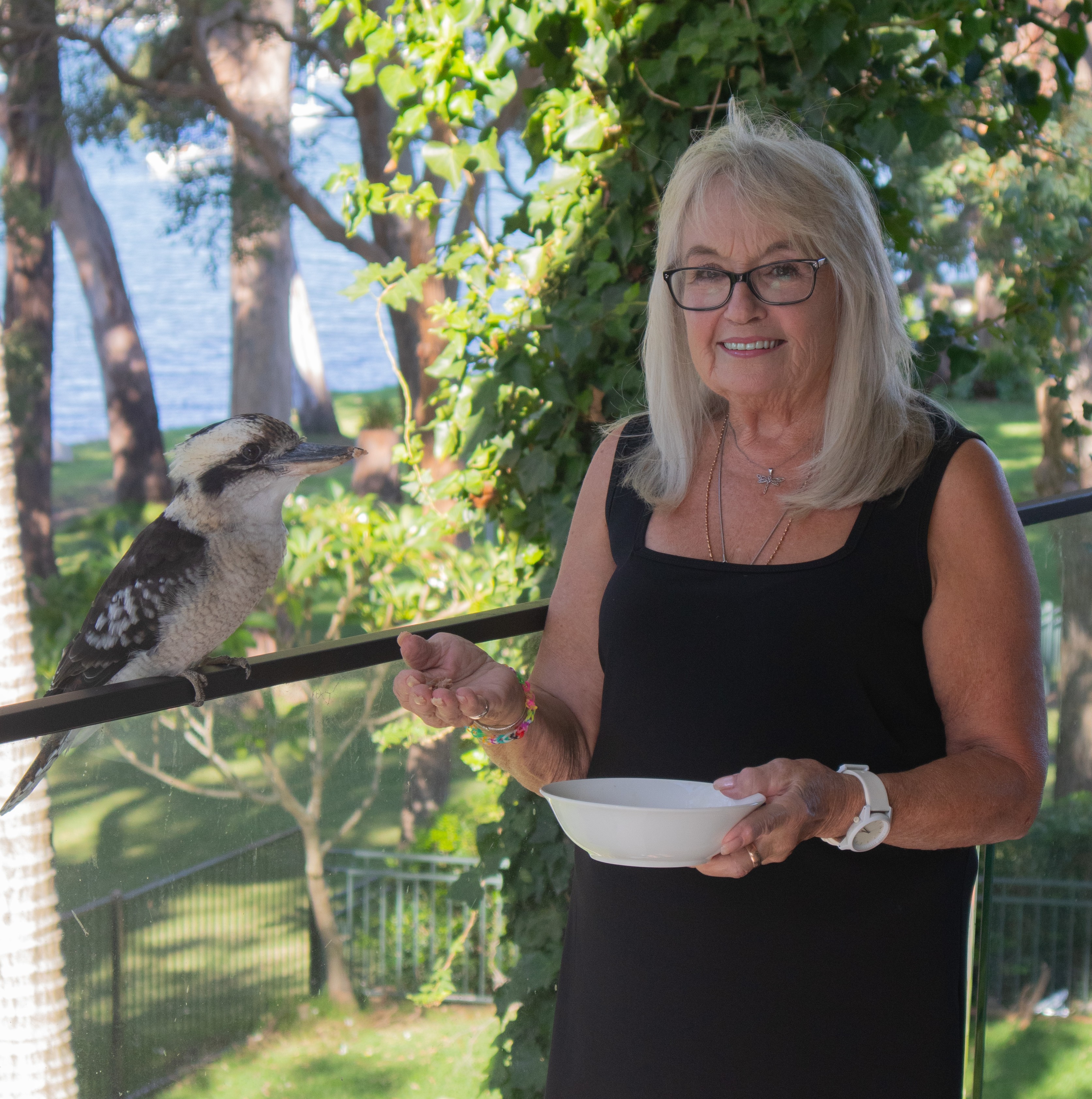 A lady wearing a black dress smiling to camera whilst feeding a Kookaburra