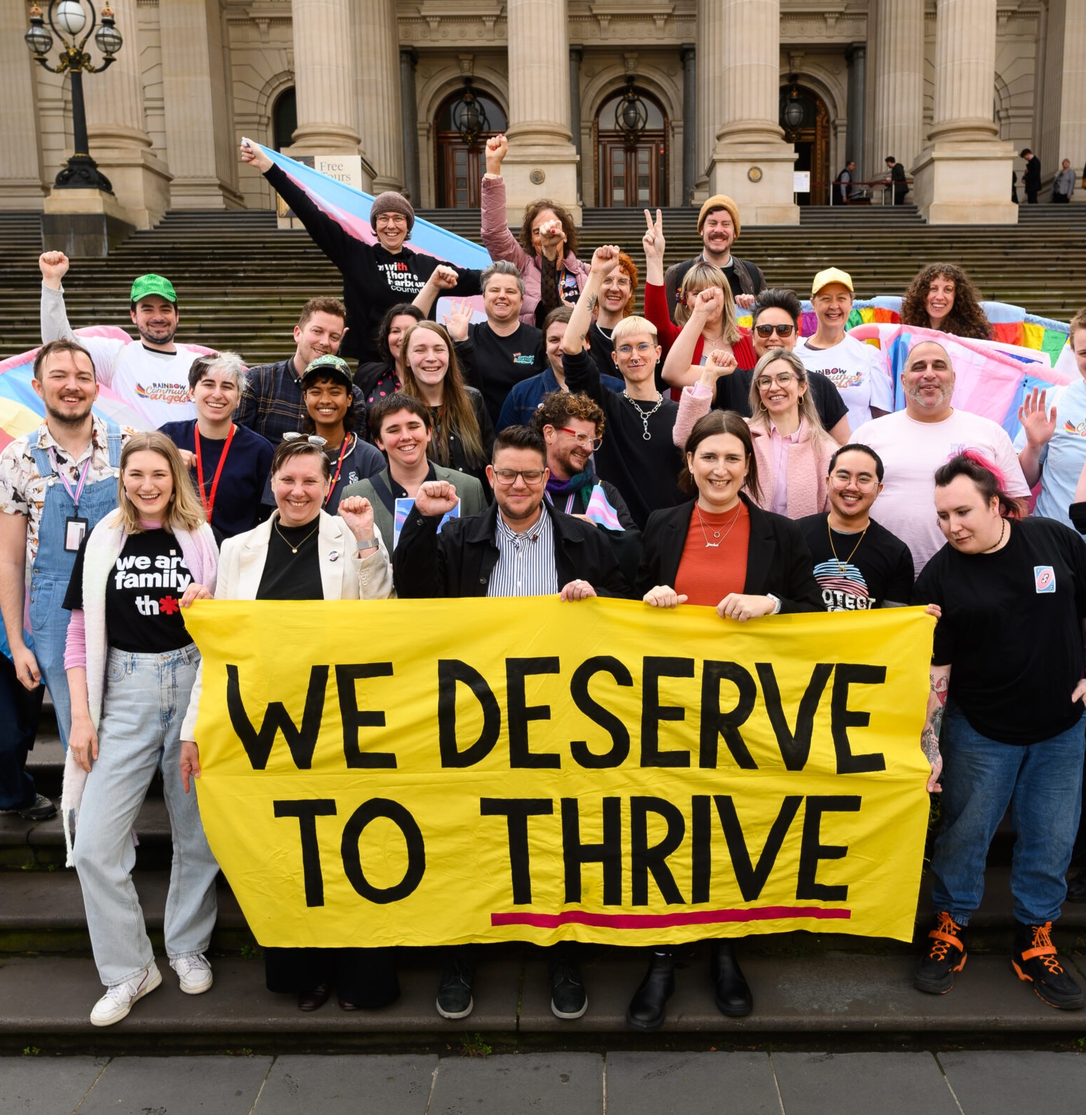 Group of people cheering behind a sign that says 'We deserve to thrive'